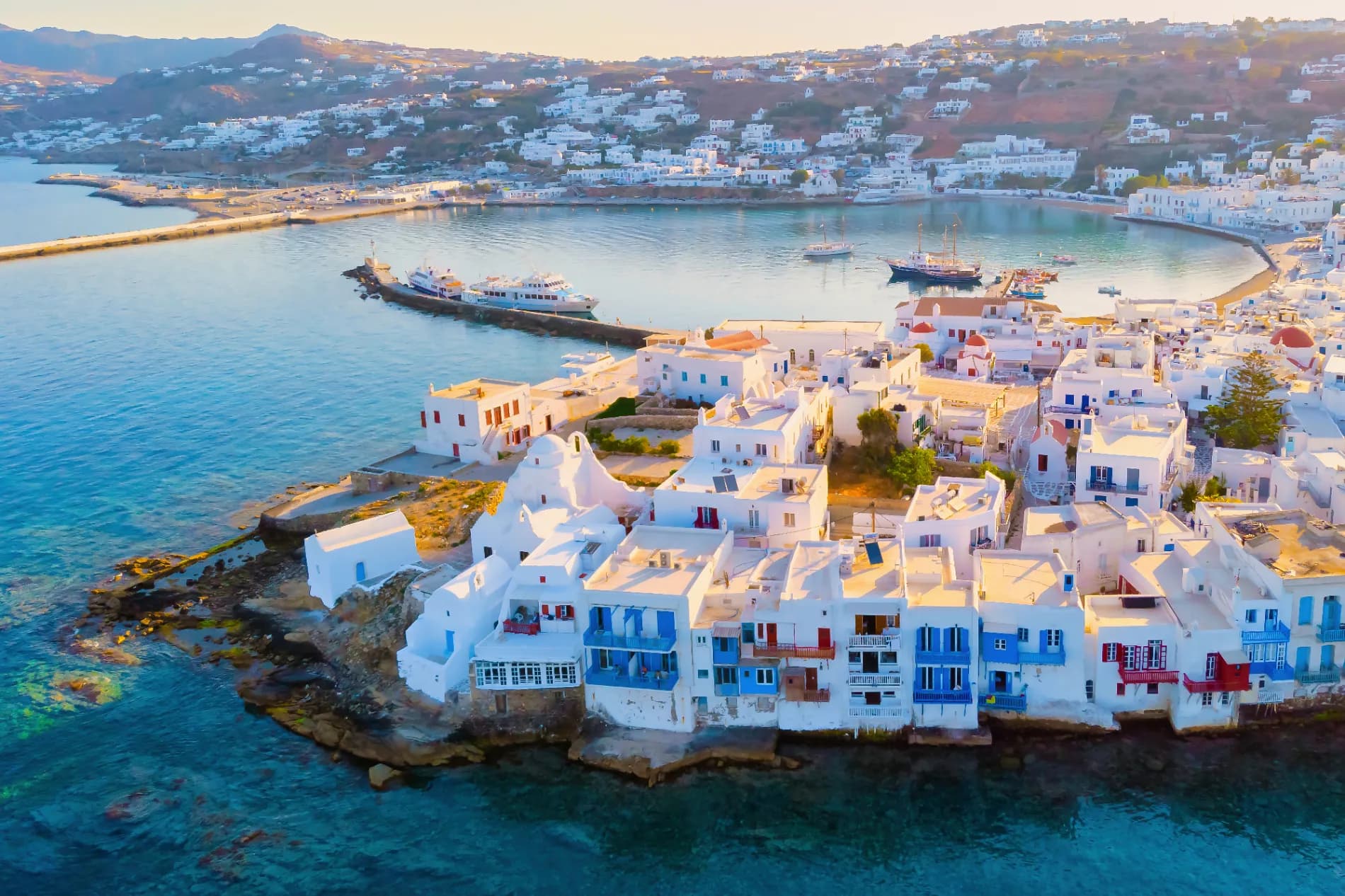 Sunlit Greek coastal village with whitewashed houses cascading toward an Aegean harbour